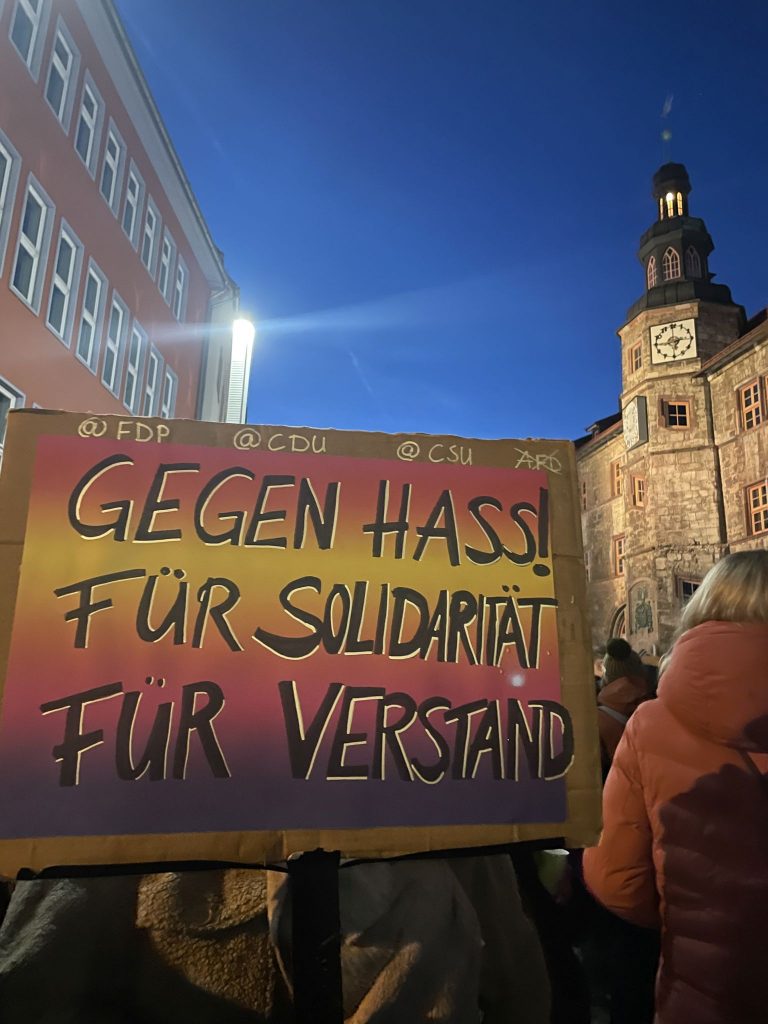 Ein hochgehaltenes Plakat: Gegen Hass! Für Solidarität - Für Verstand, Im Hintergrund rechts der Turm des Nordhäuser Rathauses.