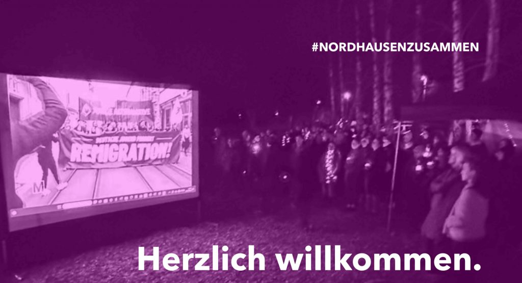 Herzlich willkommen - Menschen beim Stillen Protest in Sundhausen. Links die Leinwand mit dem projizierten Video.